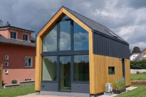 Widok na nowoczesny domek modułowy Perfect Cube w Swisttal z dużymi przeszkleniami, drewnianą elewacją oraz nowoczesnym dachem dwuspadowym.