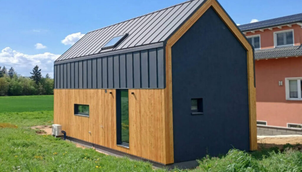 Nowoczesny dom modułowy Perfect Cube w Swisttal w Niemczech z elewacją drewnianą i grafitową blachą na rąbek w minimalistycznym stylu nowoczesnej stodoły.